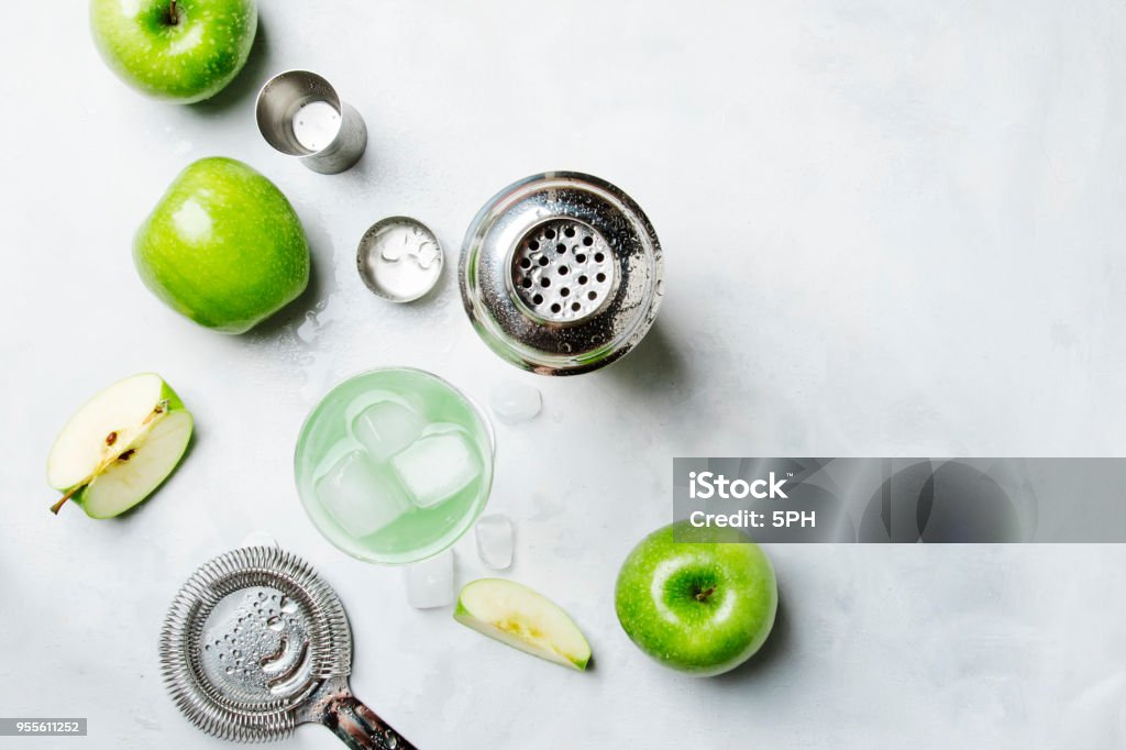 Alcoholic cocktail with green apple and dry vermouth, syrup, lemon juice and ice cubes Alcoholic cocktail with green apple and dry vermouth, syrup, lemon juice and ice cubes. Bar tools, gray stone background, top view Cocktail Stock Photo