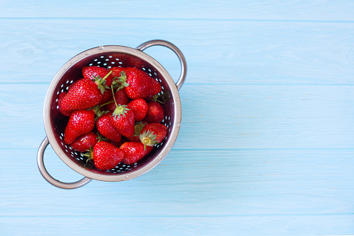 Fresh Strawberries in the Colander on Natural Blue Wood Background. Top View