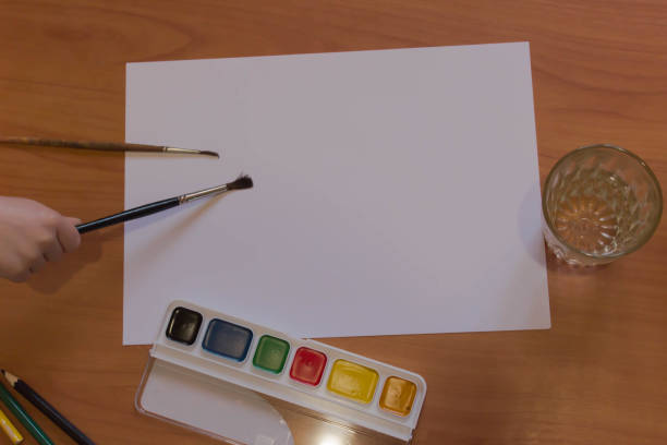 istock White sheet mock up with brushes, watercolors and child hand 955620098