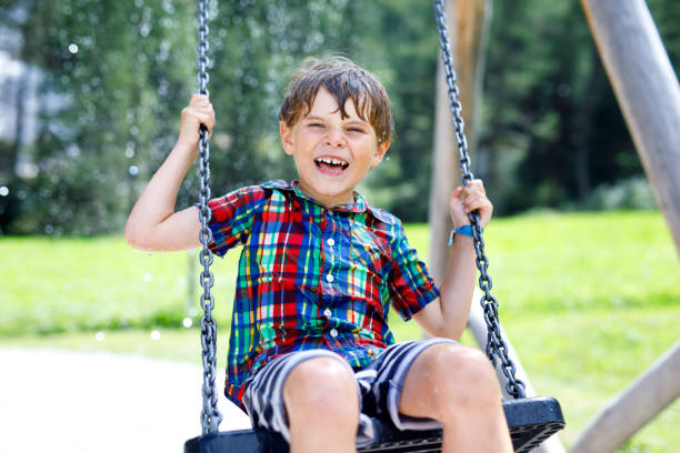 istock Funny kid boy having fun with chain swing on outdoor playground while being wet splashed with water 955627402