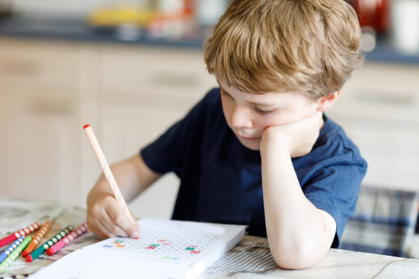 istock Tired kid boy at home making homework writing letters with colorful pens 955628298