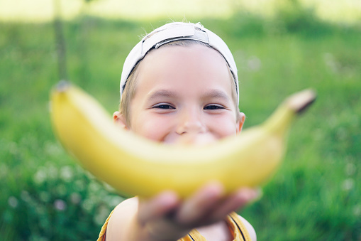Face of a beautiful young caucasian boy in cap with banana smile on nature background.