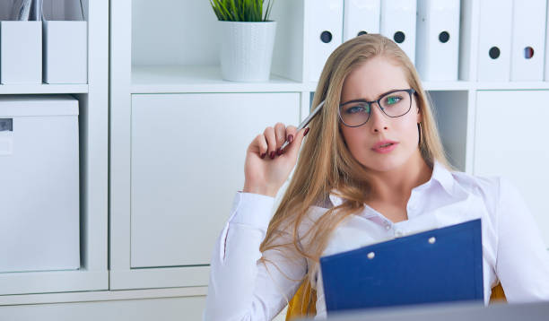 istock Young beauiful Caucasian businesswoman in glasses intently working on notebook computer and business document at office 955636484