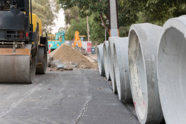 Concrete water pipes in a row with a steam roller in frame Steam roller parked near storm water pipes new big tube stock pictures, royalty-free photos & images