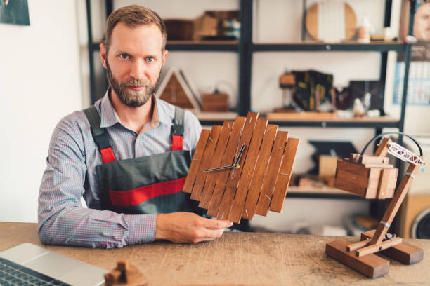 Manual worker in the carpentry showing finished wooden clock to the camera
