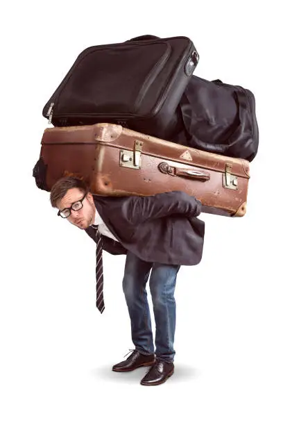 A man is straining under a heavy load of luggage. The seize of luggage is comically large.