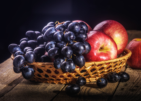 Black grapes and red apples on the table in the basket