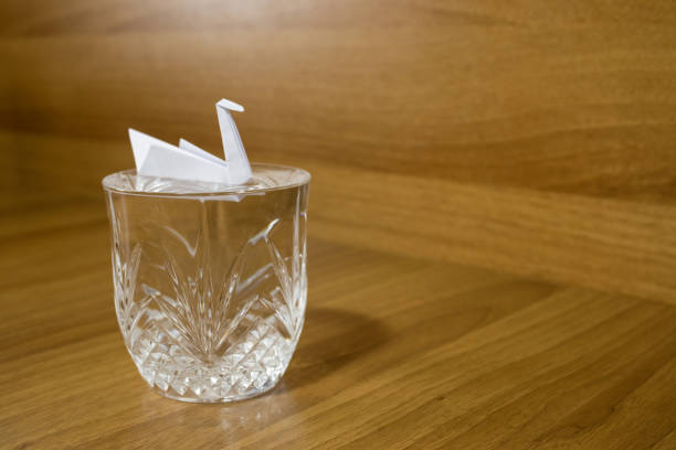 Paper crane on a crystal glass on a wood table composition