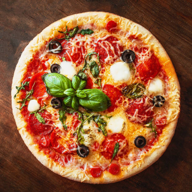 istock Hot pizza with Pepperoni  with vegetables and fresh ingredients on rustic wooden table. Pizza menu. View from above. 955669376