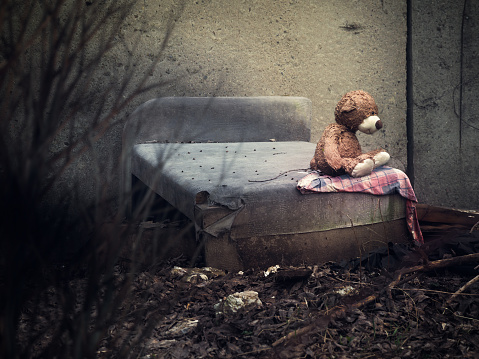 A toy bear on an old discarded bed in a dull place. The concept of homelessness, uselessness, depression