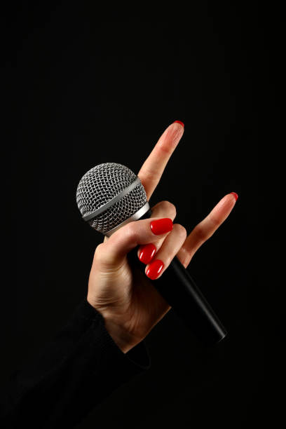 Woman hand with microphone and devil horns isolated on black Woman hand with red nails holding microphone with devil horns rock metal sign isolated on black background rocker nails stock pictures, royalty-free photos & images