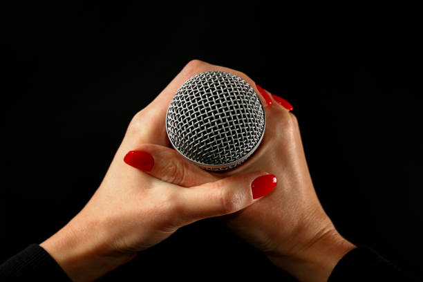Woman hands with microphone isolated on black Woman holding microphone with two hands with red nails isolated on black background rocker nails stock pictures, royalty-free photos & images