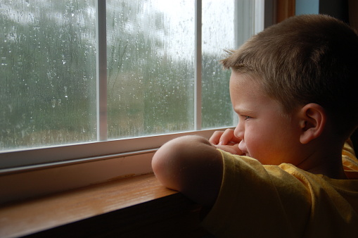 Young boy looking out a window on a rainy day.