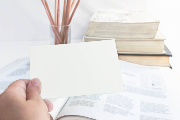 istock Education and business concept. A woman's hand hold a empty for text paper note on the open book with pile books and wooden pencil isolated on the white background. 955700630