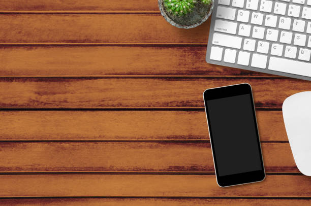 istock Wood office desk table with computer gadgets and black smartphone with blank screen. Top view with copy space, flat lay. 955719002