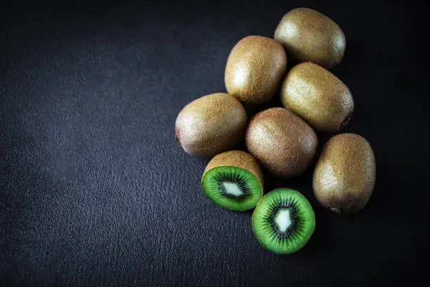 Photo of Ripe whole kiwi fruit and half kiwi fruits on black concrete   stone background, top view
