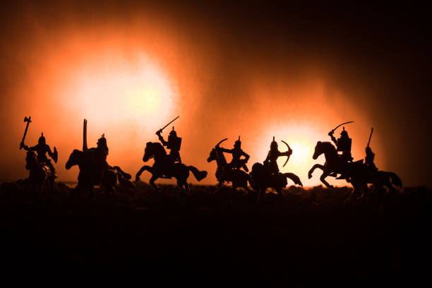 istock Medieval battle scene with cavalry and infantry. Silhouettes of figures as separate objects, fight between warriors on dark toned foggy background. Night scene. 955729322
