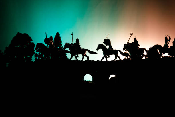 istock Medieval battle scene on bridge with cavalry and infantry. Silhouettes of figures as separate objects, fight between warriors on dark toned foggy background. Night scene. 955729584