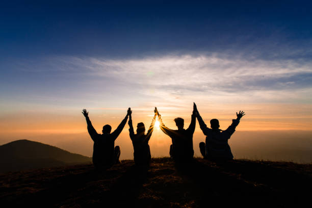 silhouette of friends shake hands up and sitting together in sunset for happiness,business successful and team work concept. silhouette of friends shake hands up and sitting together in sunset for happiness,business successful and team work concept. arms raised photos stock pictures, royalty-free photos & images