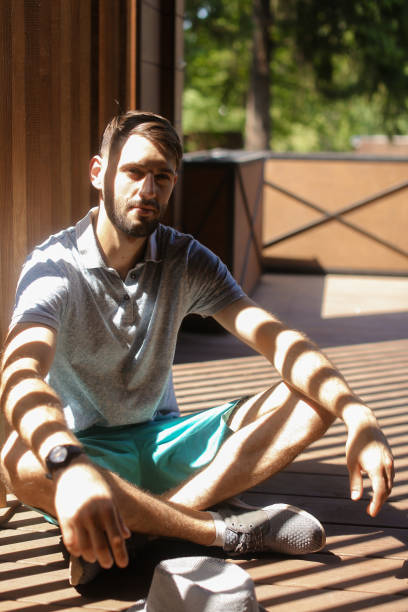 istock Handsome man in sun rays sitting on terrace and meditating, wearing shorts 955730014
