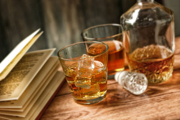 glasses of whiskey with ice and open book - selective focus - closeup
