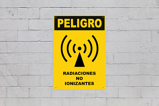 Yellow warning sign screwed to a brick wall to warn about a threat. In the middle of the panel, there is an Exclamation mark symbol and the message in Spanish saying 