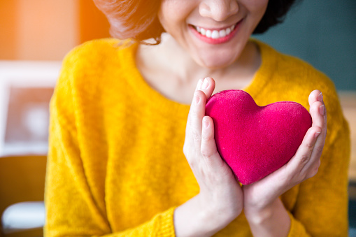 Woman  hands in yellow sweater holding pink heart.