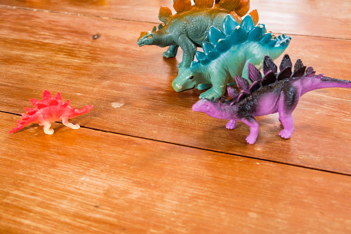 Overhead view of a collection of bright colorful Toy dinosaurs on top of a wooden table.