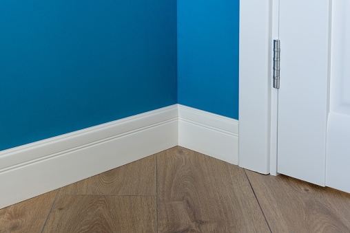 Moulding in the corner. Blue Matte Wall with laminated parquet floors immitating oak texture