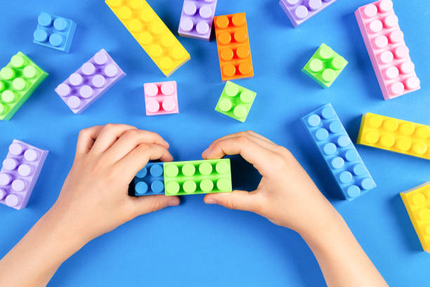 istock Kids hand playing with colorful plastic construction blocks on blue background 955784982