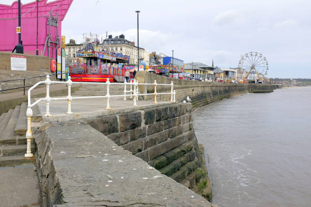 Bridlington, Yorkshire, UK. April 24, 2018. Holidaymaker walking the North beach promenade past the beach amusements at Bridlington in North Yorkshire, UK.