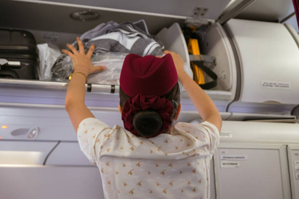 在卡塔爾航空公司的飛機上, 乘務員把行李放進頭頂的櫃子裡。 - qatar airways 個照片及圖片檔