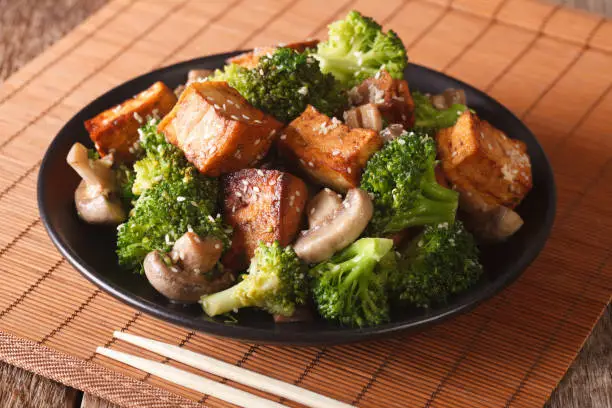 Fried tofu cheese with broccoli, mushrooms and teriyaki sauce close-up on a plate. horizontal