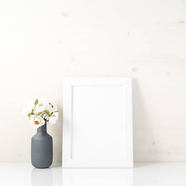 istock Blank white frame, flower in vaze on a white table against white wall with copy space. Mock up. 955795998