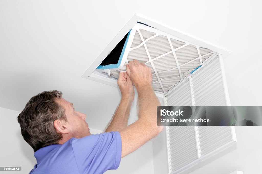 Man Removing Dirty Air Filter Mature man taking out a dirty air filter from a home ceiling air return vent. Male removing a dirty air filter with both hands in a house from a HVAC ceiling air vent. Air Duct Stock Photo