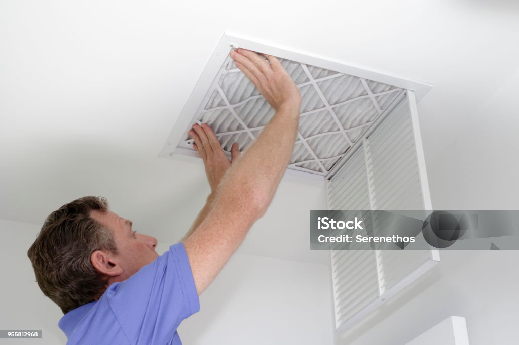 Inserting New Air Filter in Ceiling Male pushing a clean air filter into place in the ceiling with both hands. One fresh furnace air filter being secured in the intake grid of the white home ceiling. Filtration Stock Photo