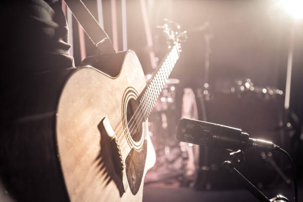 The Studio microphone records an acoustic guitar close-up, in a recording Studio or concert hall, with a drum set on a background in out-of-focus mode. Beautiful blurred background of colored lanterns