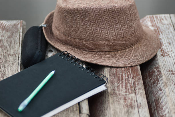 istock Black natepad, green pan, glasses case and hat on bench in park close up 955825076