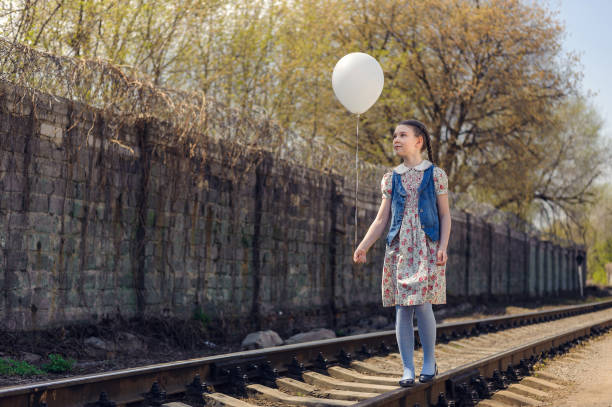 girl with pigtails walk on rails with a balloon on a string in her hand