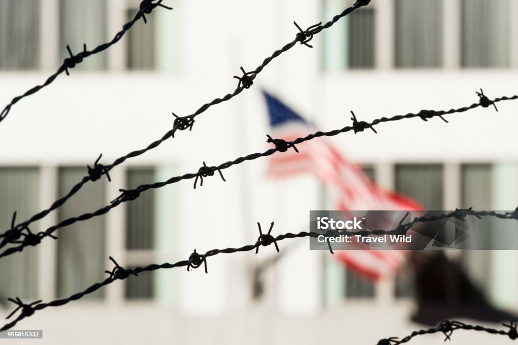 Barbed wire in the foreground and the blurred American flag in the background. Manhattan, New York city, USA. Emigration and Immigration Stock Photo