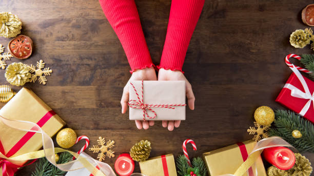 istock Hands showing Christmas gift box on wood table 955864586