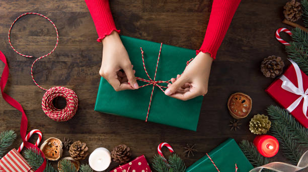 donna che lega la confezione regalo al centro degli oggetti di decorazione natalizia su un tavolo di legno - avvolto foto e immagini stock