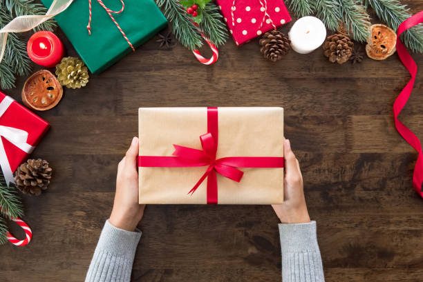 istock Woman hands showing Christmas gift box on wood table 955864668