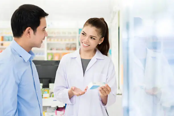 Beautiful Asian female pharmacist or doctor explaining prescription medicine to a male customer in a pharmacy.