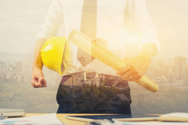 istock engineer hold security helmet and blueprint paper construction drawing plan near laptop computer,Architect working in office,Engineering tools on desk at site project,double exposure ,vintage color 955879588