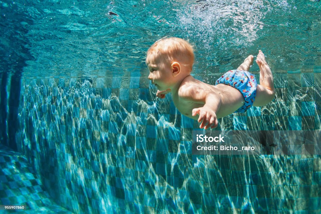 Child jump underwater into swimming pool Happy child learn to swim, dive in blue pool with fun - jumping deep down underwater with splashes. Healthy family lifestyle, kids water sports activity, swimming lesson with parents in fitness club Baby - Human Age Stock Photo