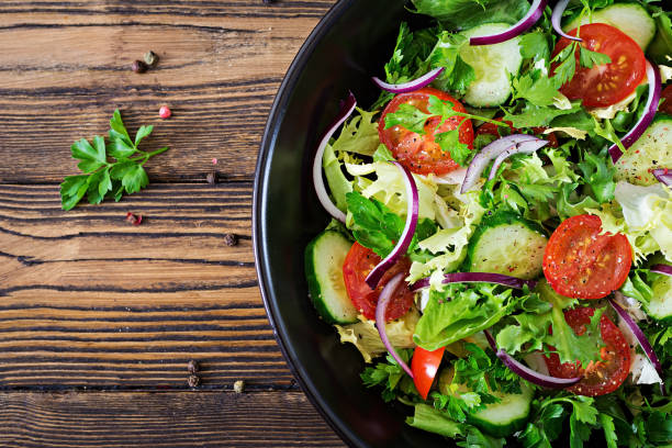 Salad from tomatoes, cucumber, red onions and lettuce leaves. Healthy summer vitamin menu. Vegan vegetable food. Vegetarian dinner table. Top view. Flat lay stock photo