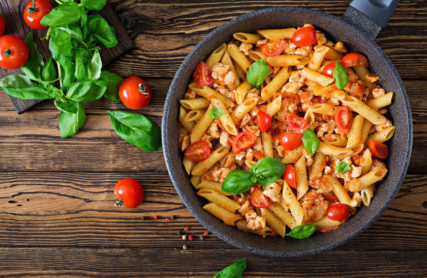 istock Penne pasta in tomato sauce with chicken, tomatoes, decorated with basil on a wooden table. Italian food. Pasta Bolognese. Top view. 955920746
