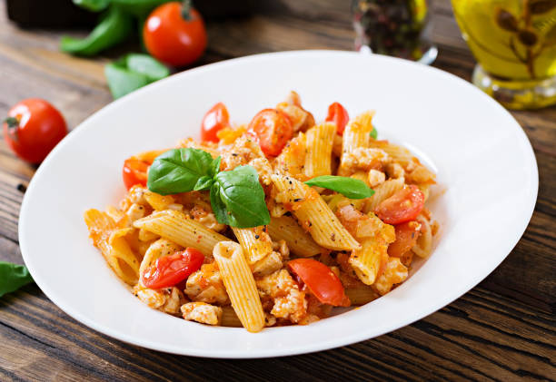 istock Penne pasta in tomato sauce with chicken, tomatoes, decorated with basil on a wooden table. Italian food. Pasta Bolognese. 955920748