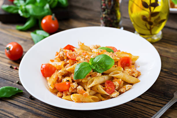 istock Penne pasta in tomato sauce with chicken, tomatoes, decorated with basil on a wooden table. Italian food. Pasta Bolognese. 955920764